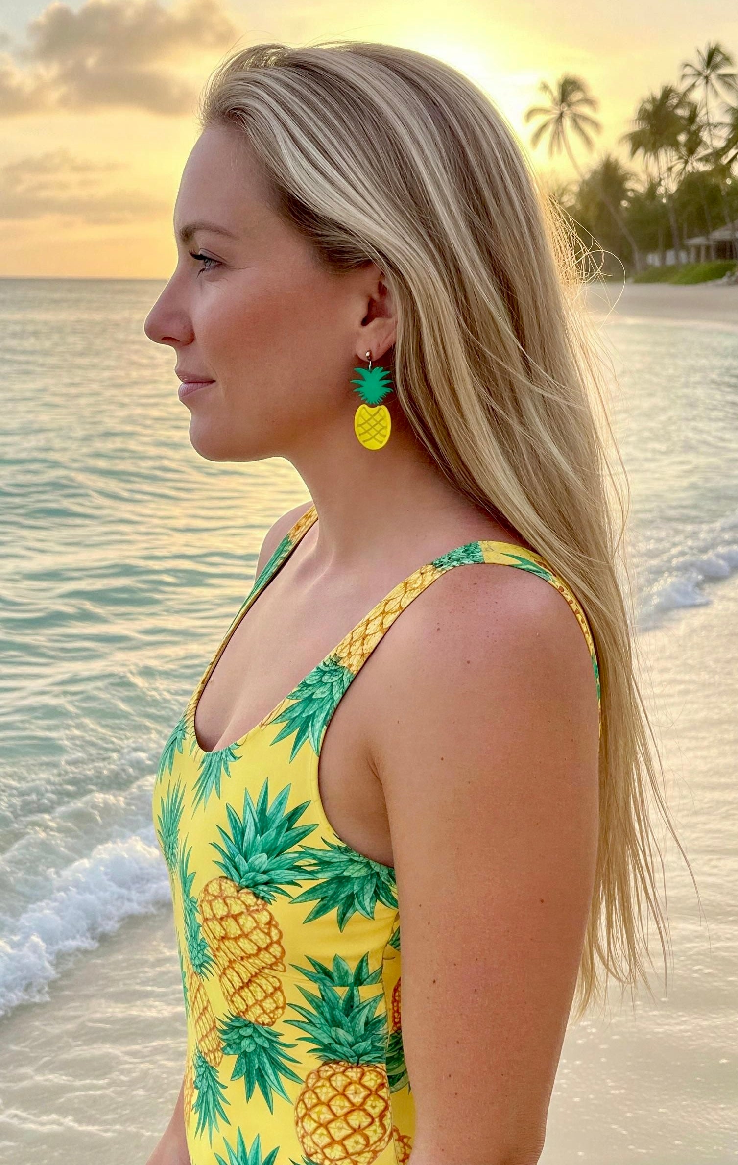 Woman wearing a yellow swimsuit with pineapple pattern on a beach at sunset.